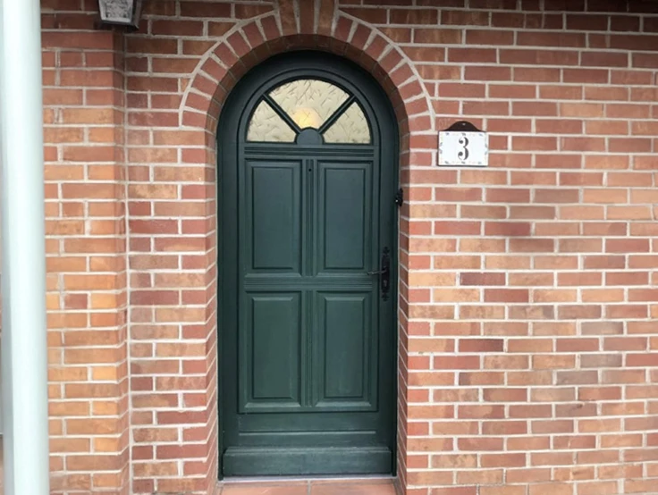 Intérieur d'habitation avec porte d'entrée sécurisée ouverte, mur en briques apparentes, sol carrelage