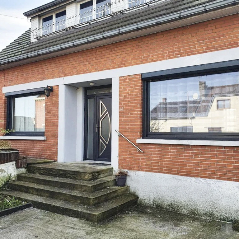 Façade extérieure d'habitation avec porte d'entrée blanche ornée de vitraux décoratifs et deux fenêtres à volets roulants partiellement fermés