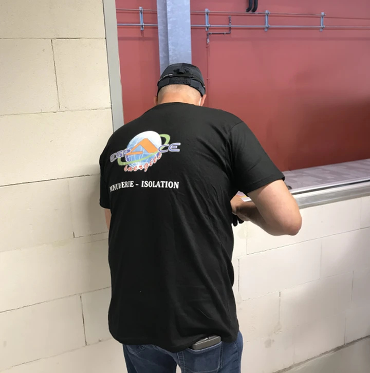 Un professionnel en tenue de travail applique un joint d'étanchéité silicone blanc autour d'une fenêtre PVC à l'aide d'un pistolet à cartouche